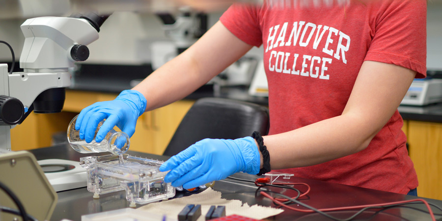 Student wearing Hanover College t-shirt using science lab equipment